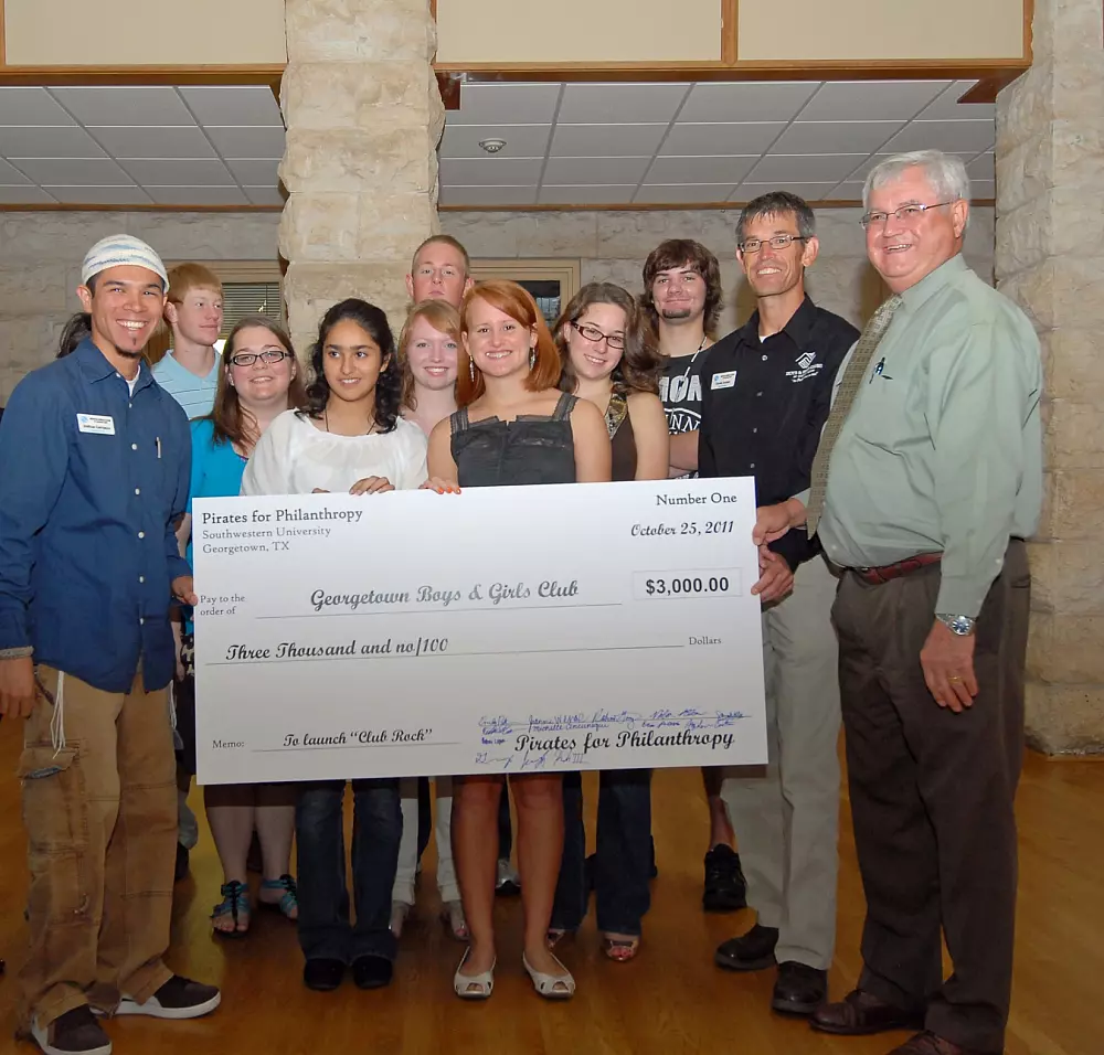A group of Southwestern University students and representatives pose indoors holding a large $3,000 donation check from Pirates for Philanthropy to the Georgetown Boys & Girls Club.